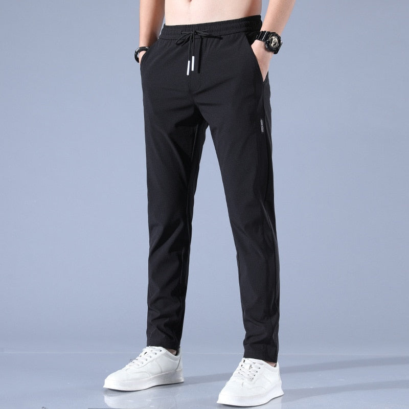 Lichtgrijze sportbroek voor heren, met elastische tailleband en trekkoord, gecombineerd met witte sneakers. Comfortabele en stijlvolle sportkleding.